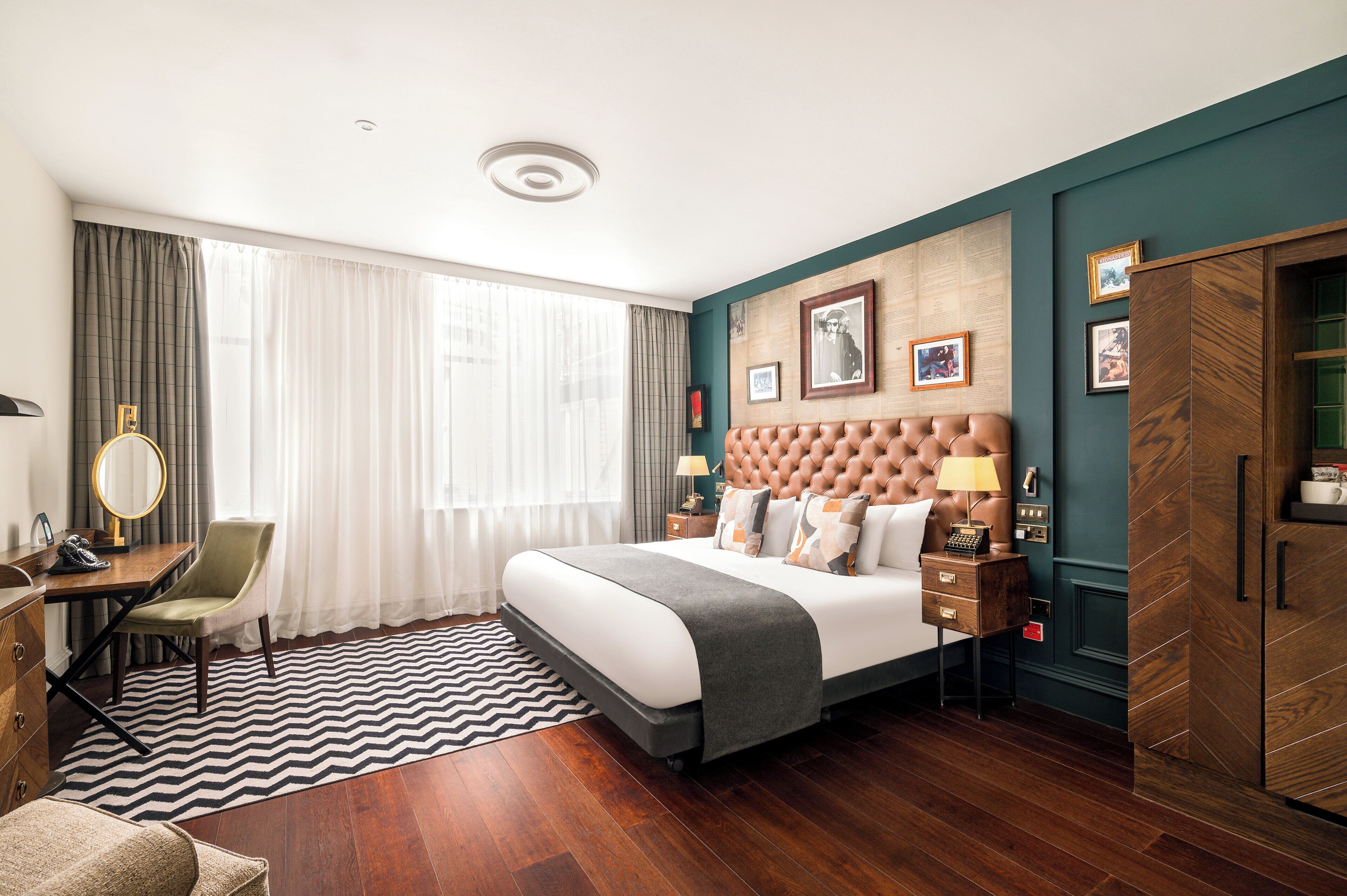 A hotel room with a large bed, a desk with a chair, a wardrobe, and a window with curtains.