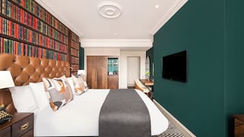 A bedroom with a large bookshelf, a tufted headboard, a flat-screen TV, and a view of a green outdoor area.