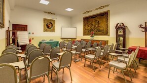 A conference room with rows of chairs, a whiteboard, a projector screen, a clock, and a large tapestry.