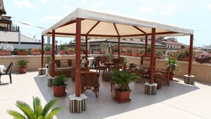 A rooftop patio with outdoor seating, potted plants, and a pergola structure.