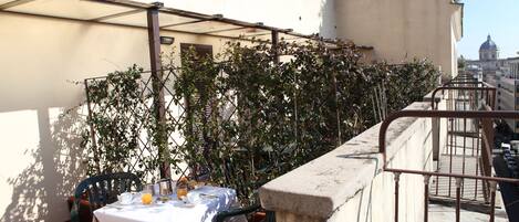 A rooftop terrace with a table set for two, surrounded by greenery and overlooking a cityscape.