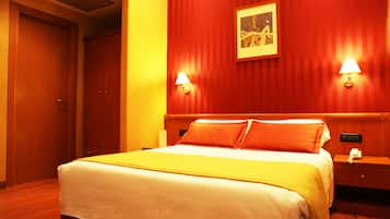 A hotel room with a bed, wooden headboard, two bedside lamps, a nightstand, and a framed picture on the wall.