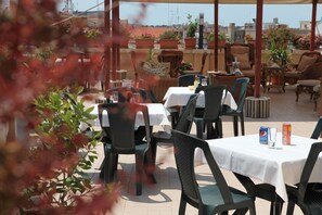 Un área de comedor al aire libre con mesas y sillas, plantas en macetas y vistas a la ciudad.