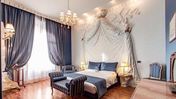 A bedroom with a canopy bed, two bedside tables with lamps, a chair, and a desk.