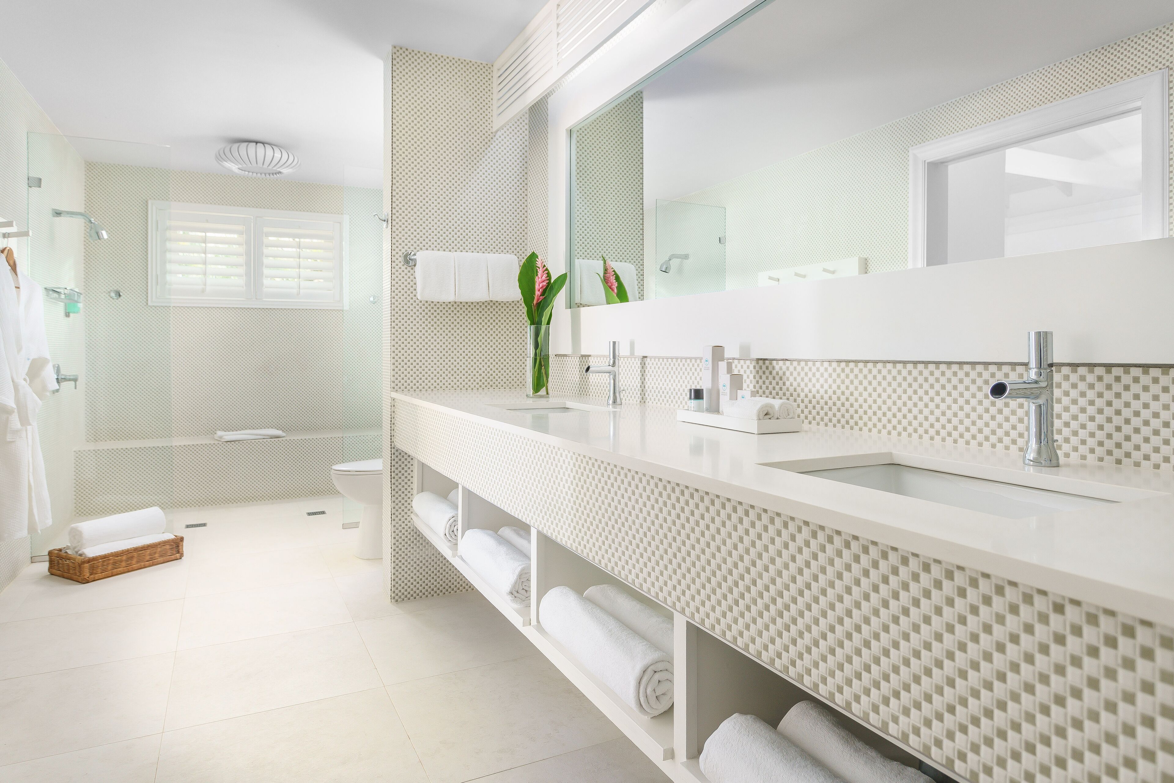 A modern bathroom with a large mirror, white sink, and a shower area.