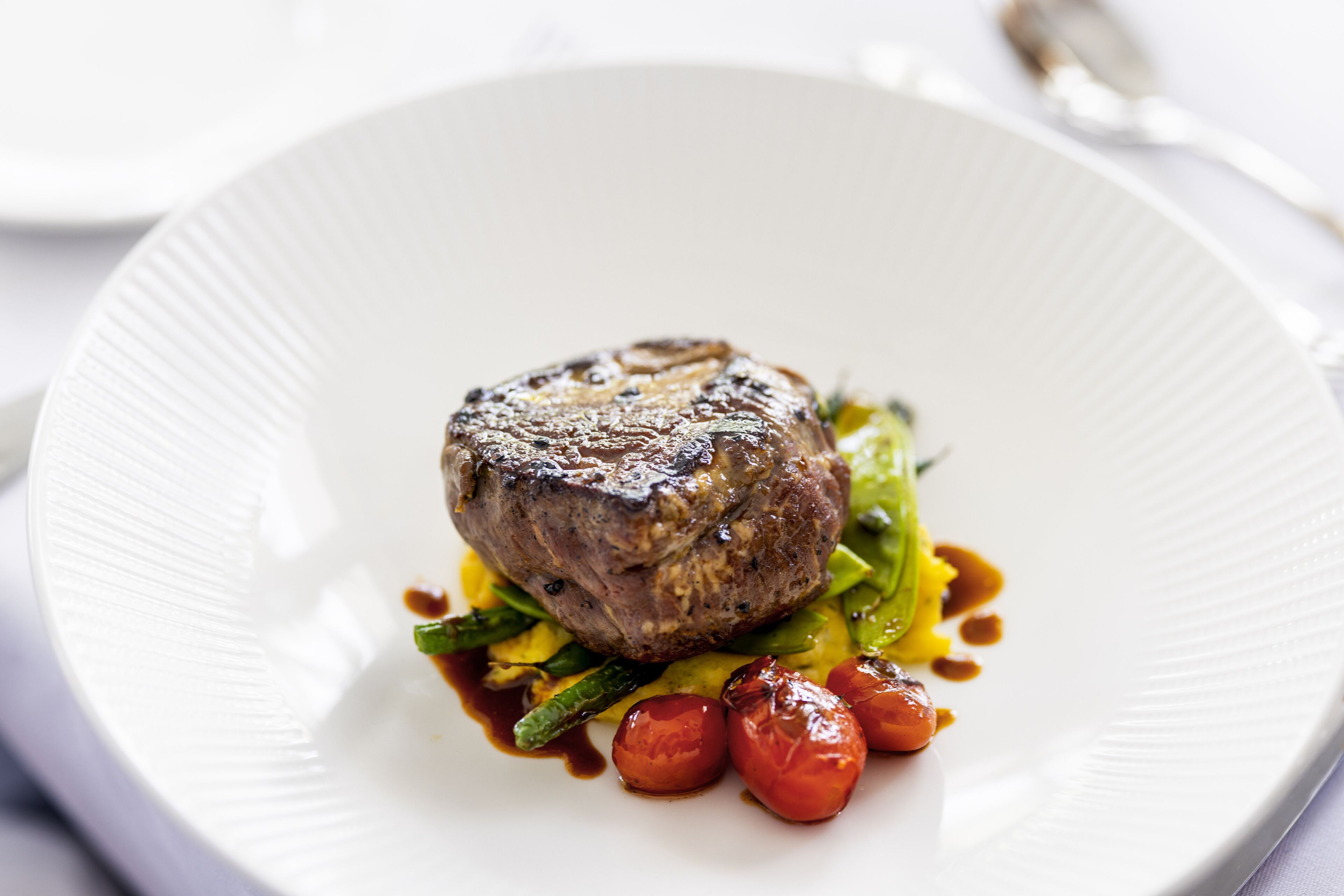 A white plate with a steak, green vegetables, and roasted tomatoes.