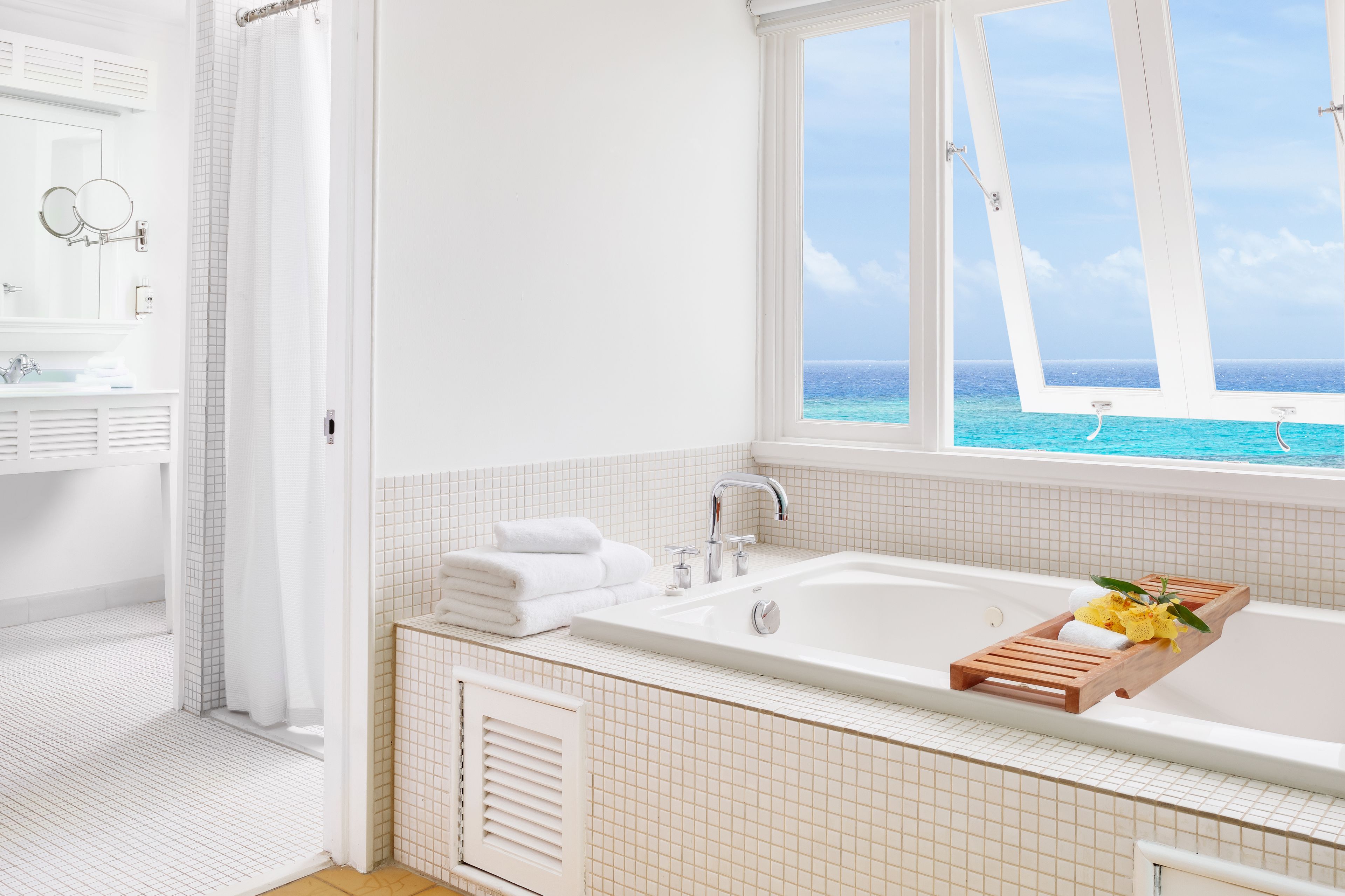 Un baño moderno con una bañera grande, un ventanal con vista al océano y un tocador con espejo y toallero.