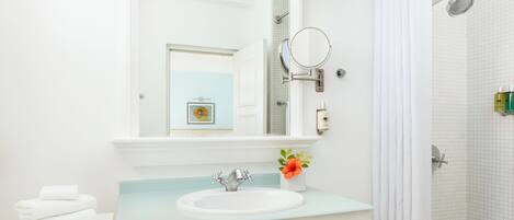 Un baño con lavamanos blanco, un espejo, ducha y toallero.