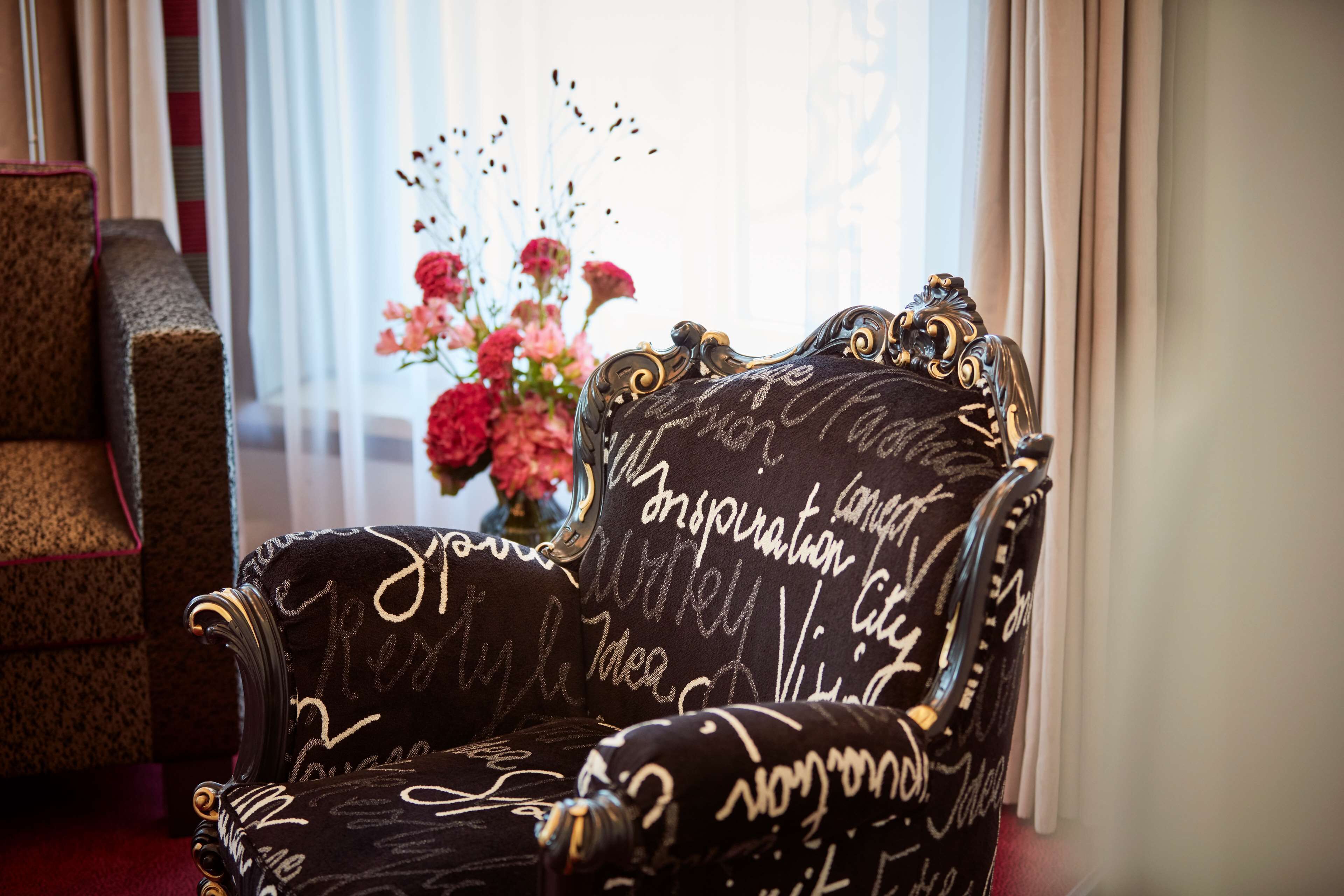 A chair with ornate carvings and a floral arrangement in the background.