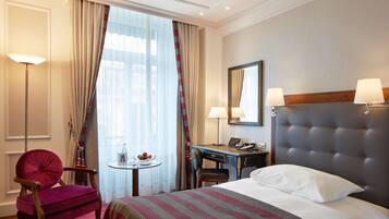 Ein Hotelzimmer mit Bett, Schreibtisch, Stuhl, kleinem Tisch und einem Fenster mit Vorhängen.