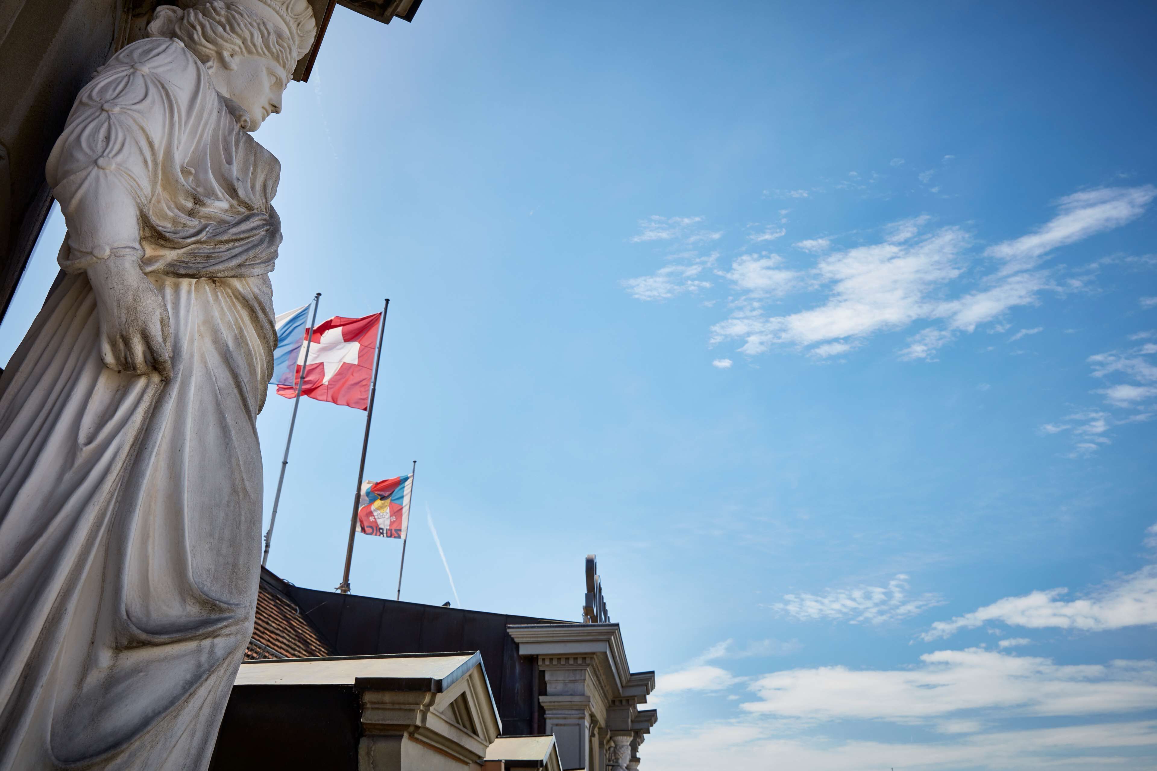 A statue of a classical figure, a building with classical architecture, and two flags.