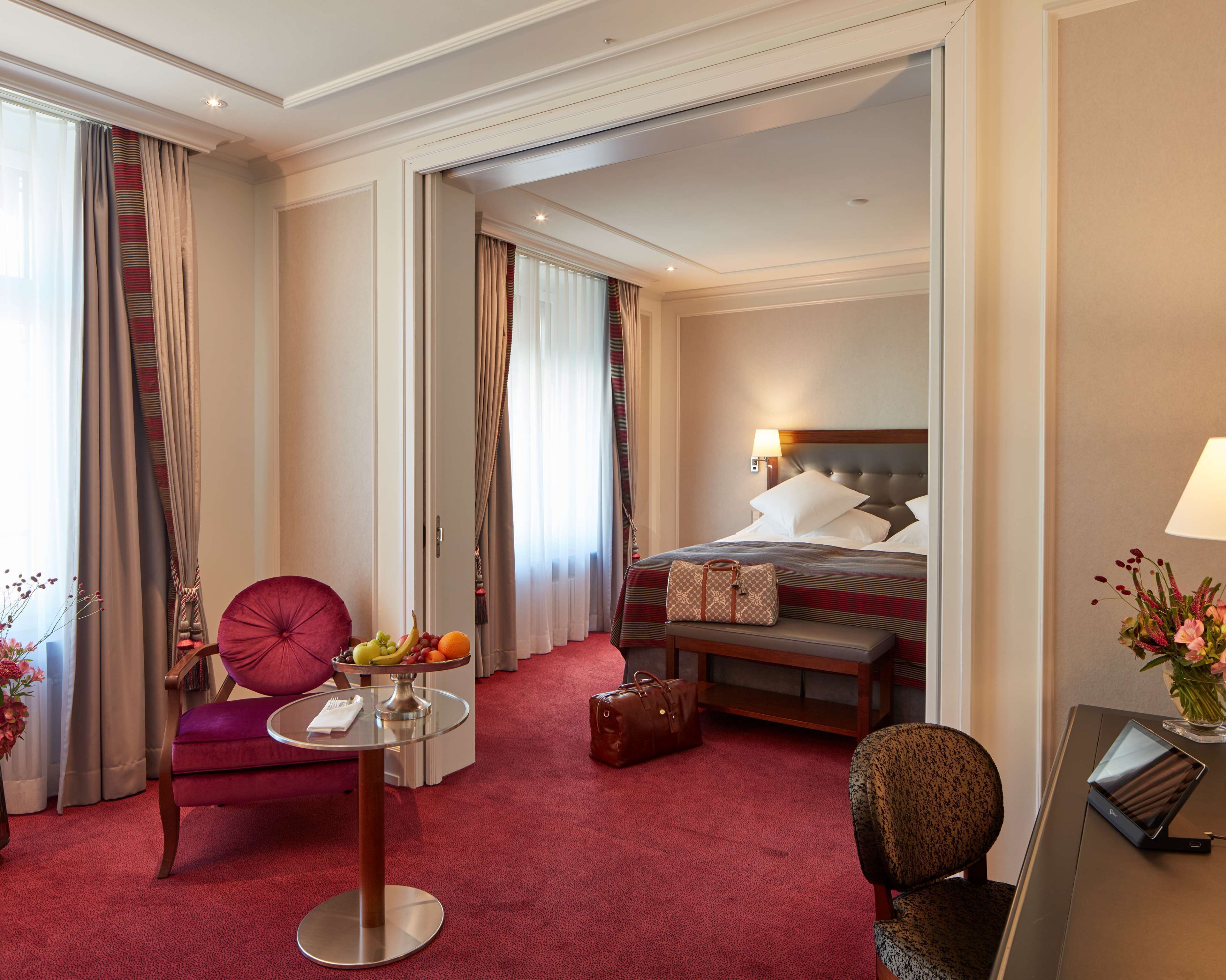 Une chambre d’hôtel avec un lit, un bureau, une chaise, une table avec des fruits et une valise.