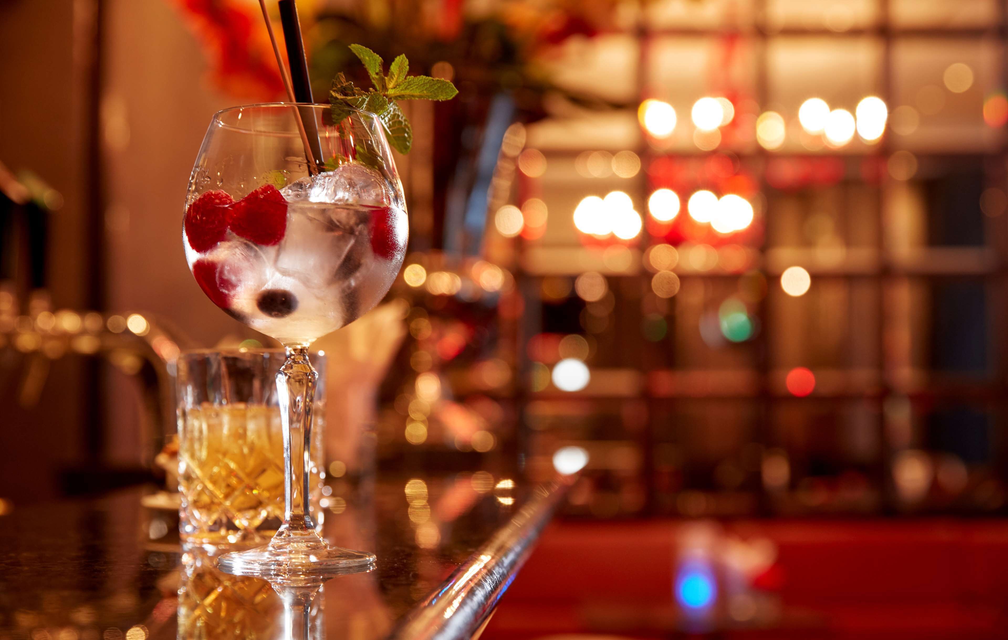 Un bar con una copa de cóctel adornada con fresas y menta, y una copa de whiskey.