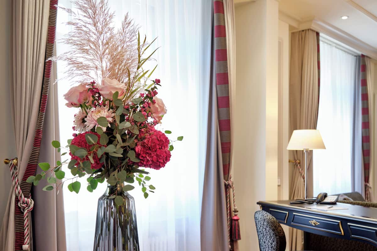 A hotel room with a desk, chair, and a vase of flowers on a table.