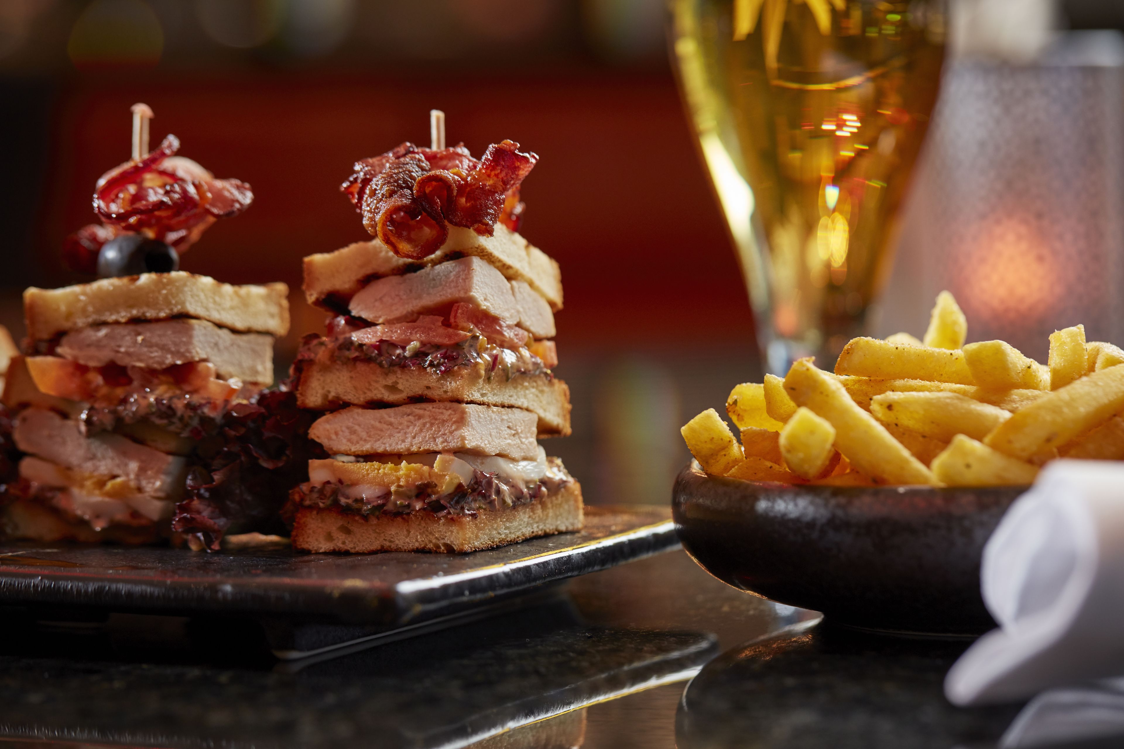 A sandwich with bacon and a bowl of fries on a table.