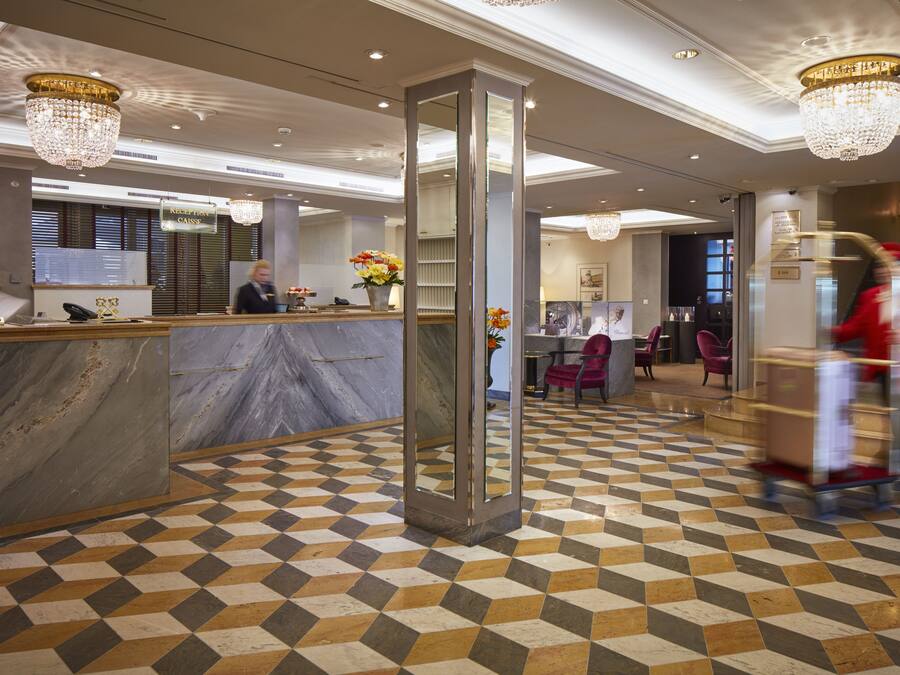 Eine Hotelhalle mit einer Rezeption, einem großen Spiegel und einem gemusterten Boden.