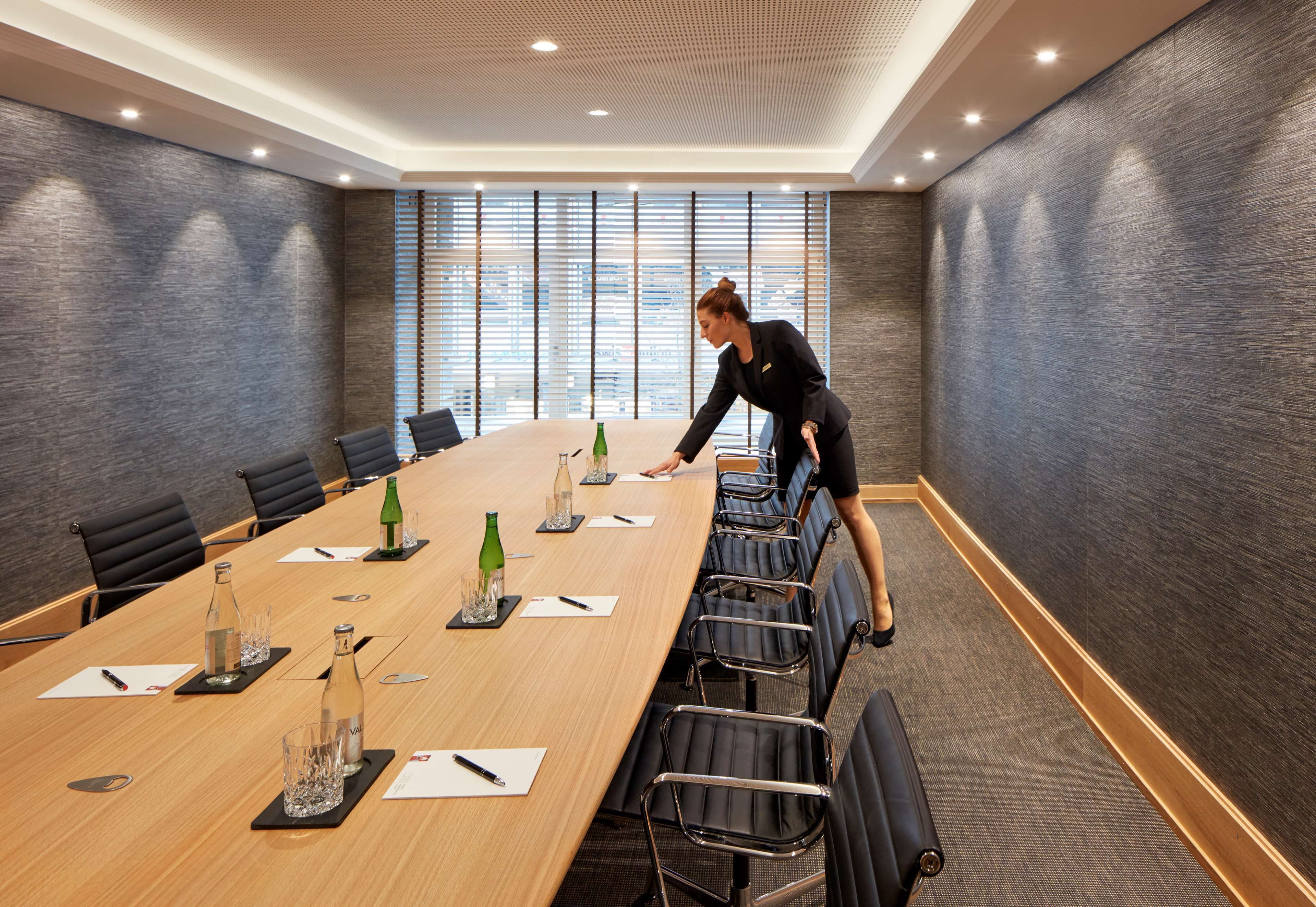 A conference room with a long table, chairs, and a person arranging items.