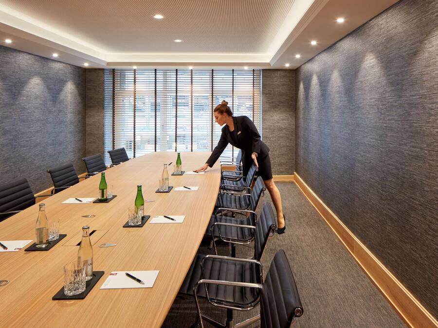 A conference room with a long table, chairs, and a person arranging items.