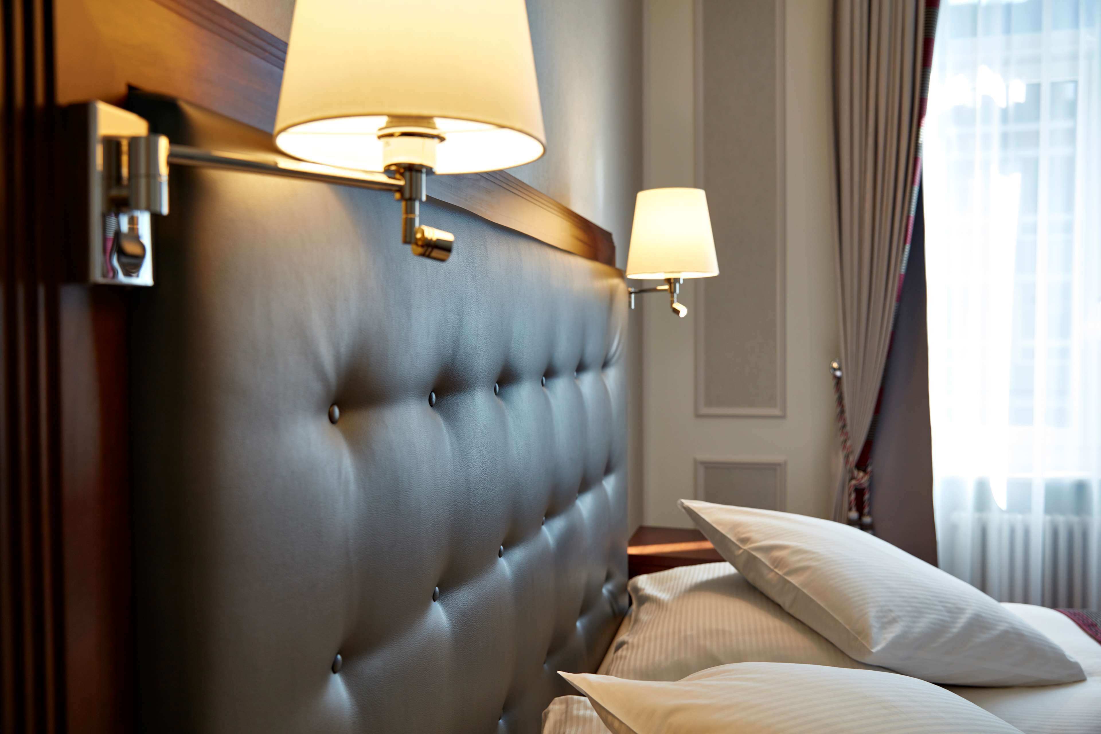 A hotel room with a tufted headboard, two bedside lamps, a bed with white linens, and a window with curtains.