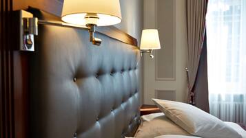 A hotel room with a tufted headboard, two bedside lamps, a bed with white linens, and a window with curtains.