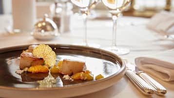 A plated dish with seared scallops and citrus garnish on a reflective plate, accompanied by a folded napkin and a fork.
