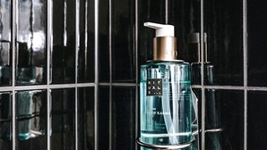 A bathroom with a black tiled wall and a glass bottle of Rituals shower gel.