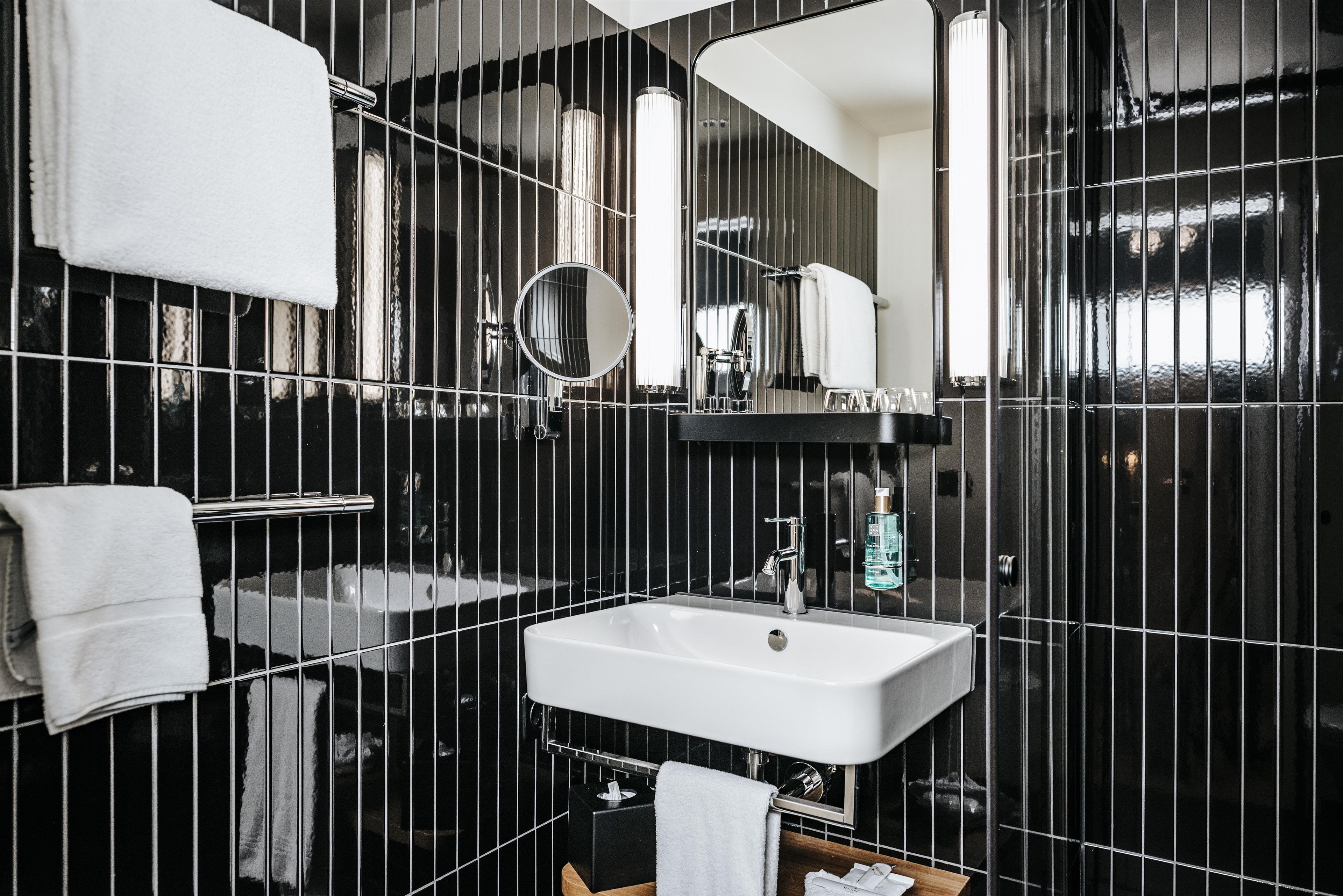 Un baño moderno con un lavamanos blanco, un espejo y paredes con azulejos negros.