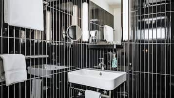 Un baño moderno con un lavamanos blanco, un espejo y paredes con azulejos negros.