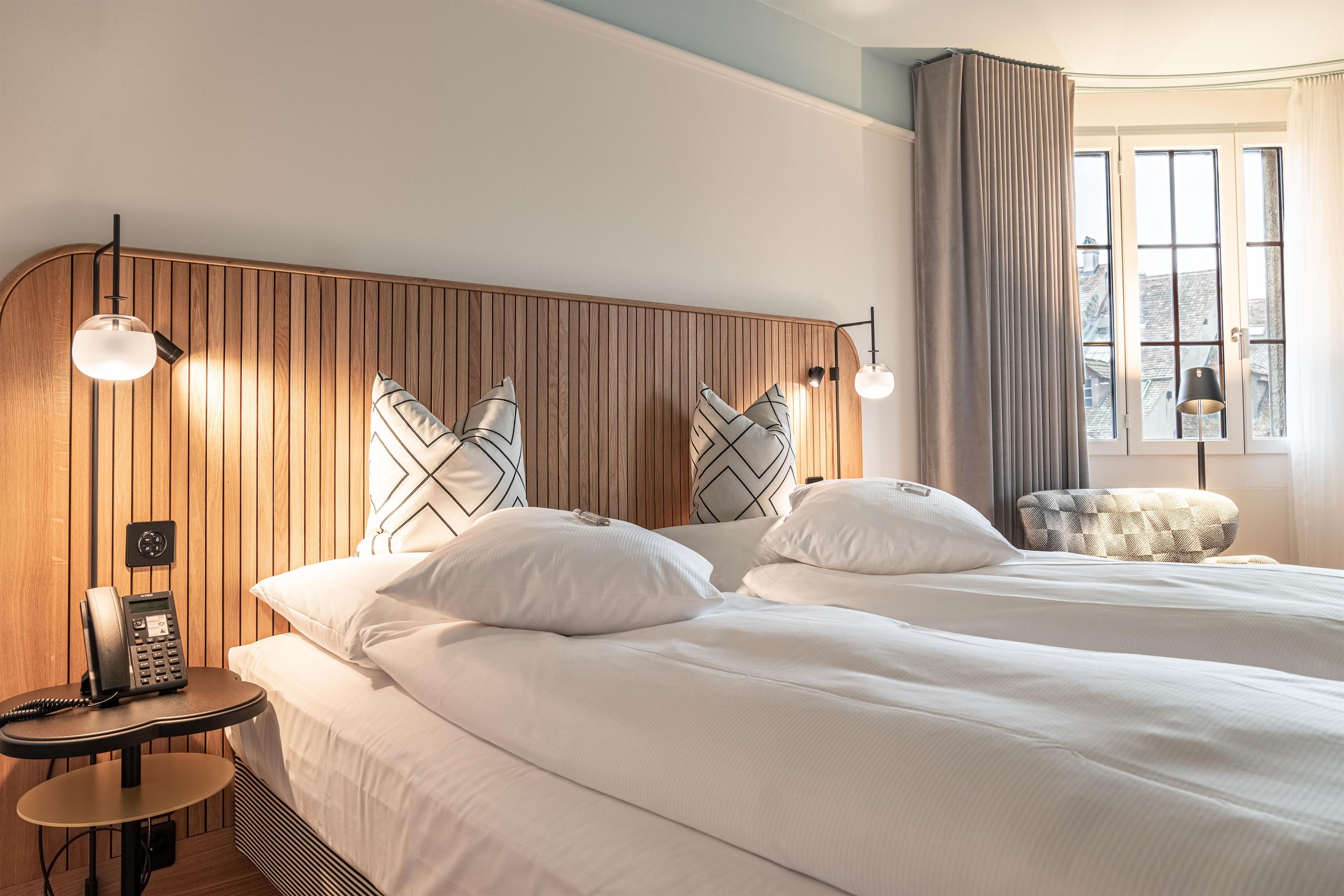 Habitación de hotel con dos camas, un teléfono, una mesita y una ventana con cortinas.