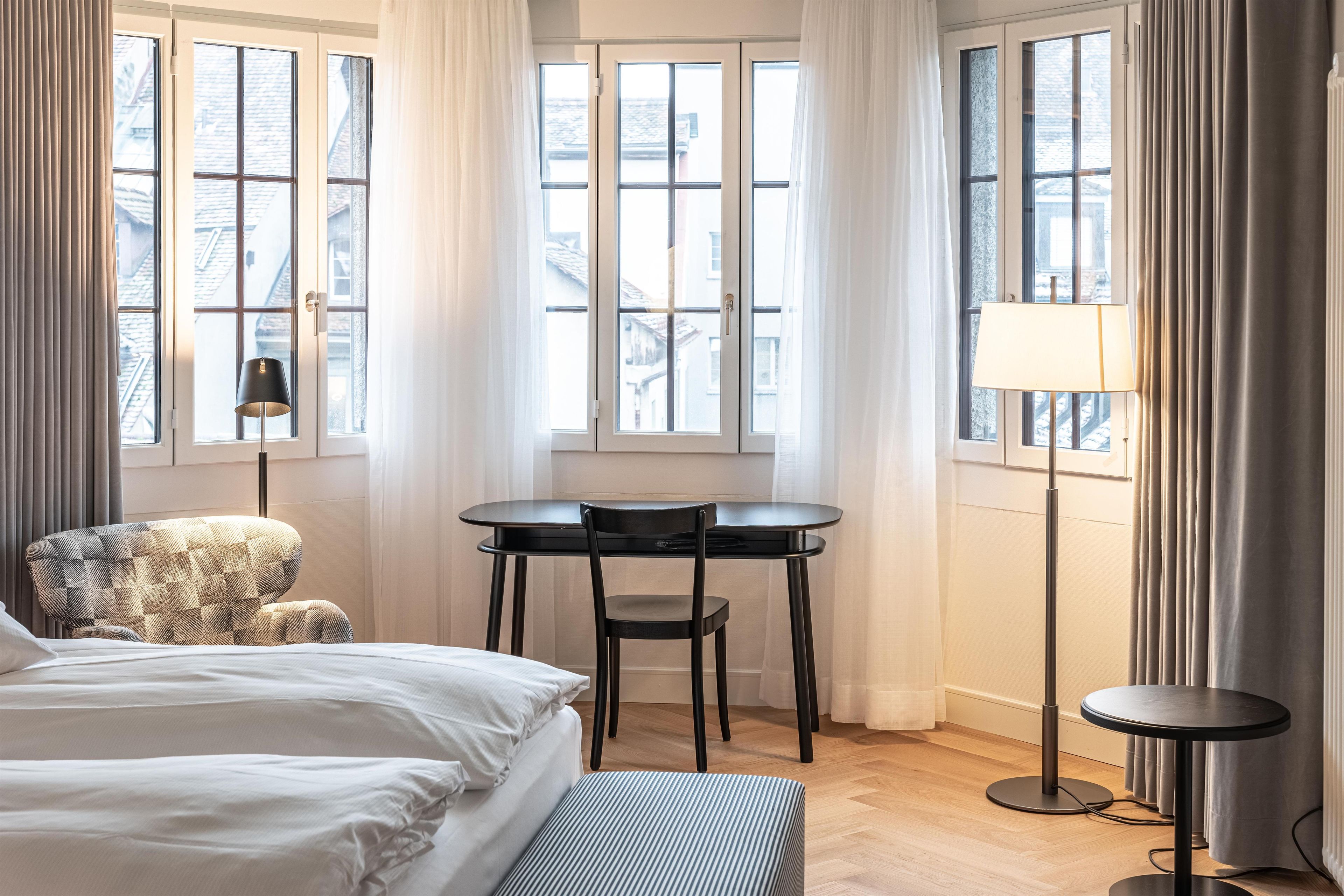 Una habitación de hotel con una cama, una silla, una mesa y una lámpara.