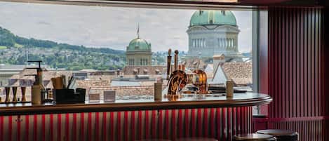 A bar with stools, a view of a cityscape, and a chandelier.