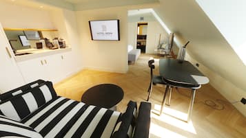 Een moderne hotelkamer met een kitchenette, een eethoek met een tafel en stoelen, een gestreepte bank en een logo in een lijst aan de muur.