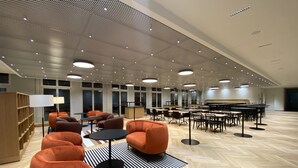 A spacious room with modern furniture, including orange chairs and tables, a piano, and a bookshelf.