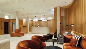 A modern lobby with a reception desk, seating areas, and a wooden accent wall.