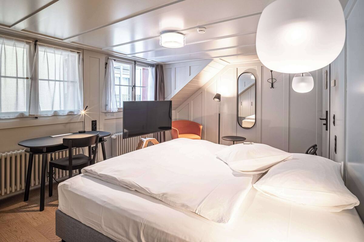 Una habitación de hotel moderna con una cama grande, un escritorio con una silla, un televisor y una mesita.