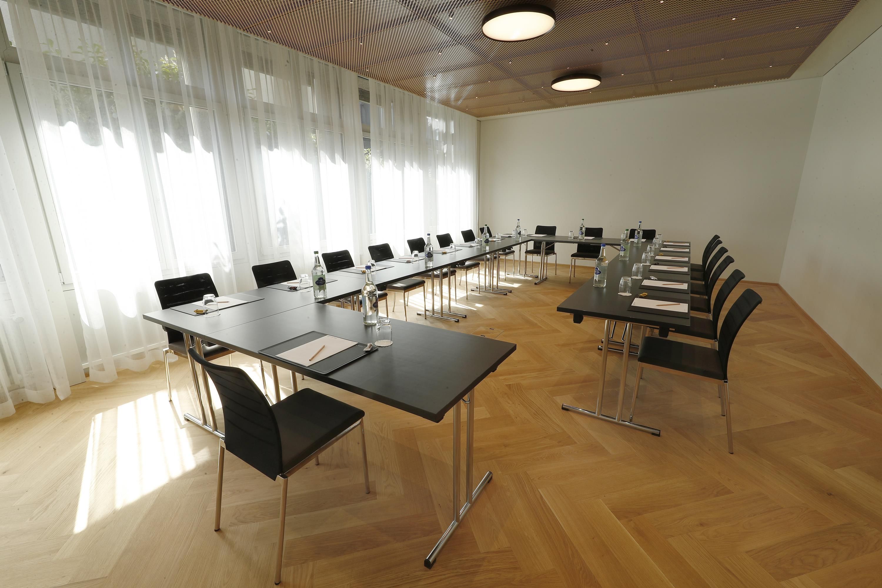 A conference room with long tables, chairs, and a wooden floor.