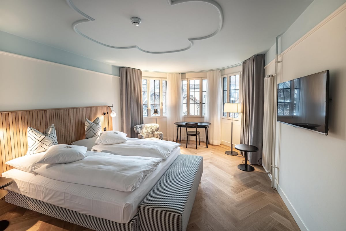 A hotel room with a large bed, a desk, a chair, and a TV.