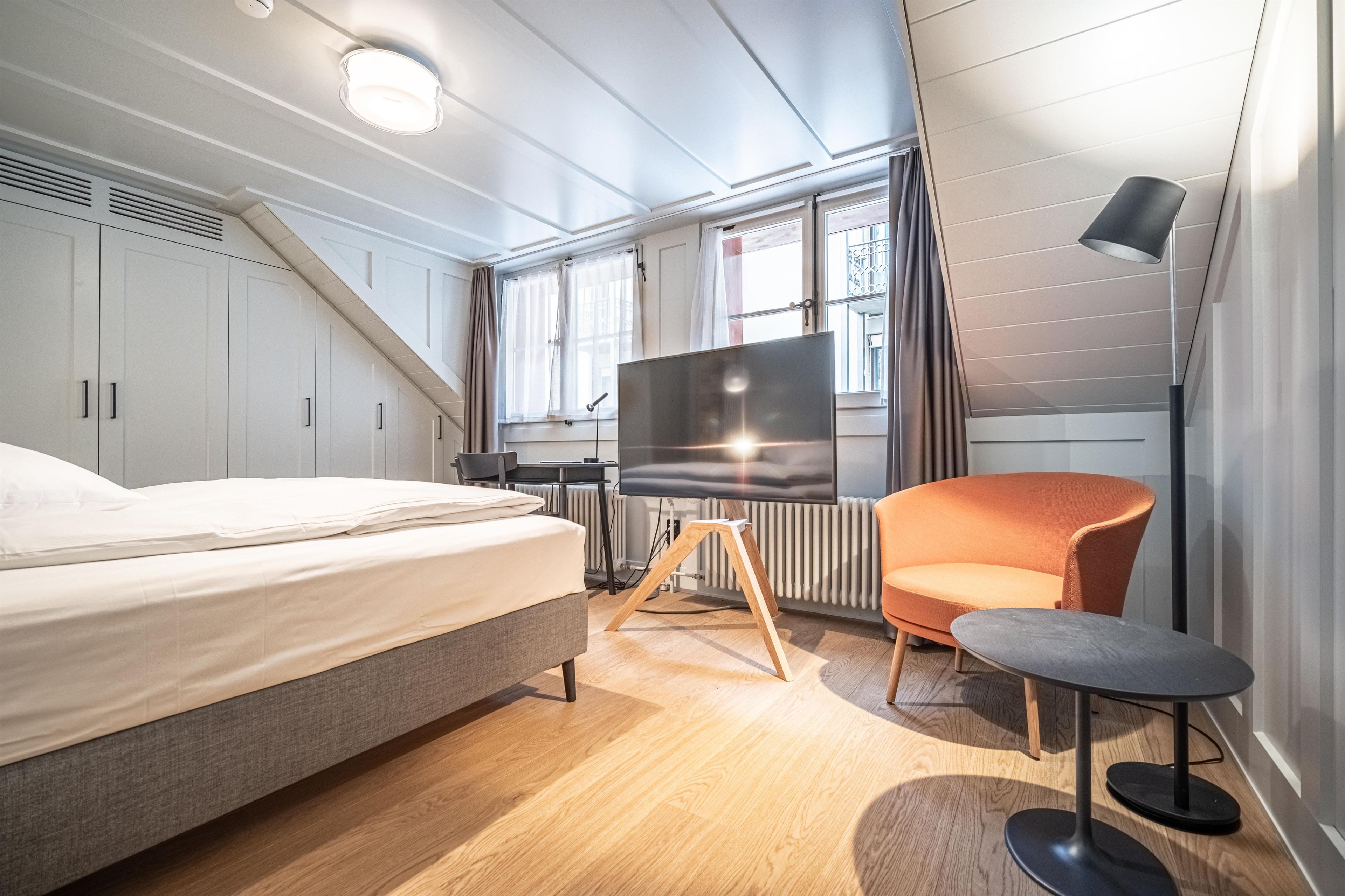A modern hotel room with a bed, a TV on a wooden stand, a small table, and a chair.