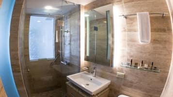 Un baño moderno con cabina de ducha de vidrio, un espejo grande y un tocador con lavabo.