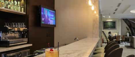 A bar area with a drink on the counter, a television mounted on the wall, and a staircase in the background.