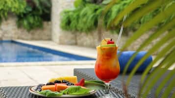 Un décor tropical avec une piscine, une assiette de fruits et un verre à cocktail.