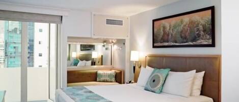 A hotel room with a large bed, a balcony, a painting on the wall, and a view of the city.