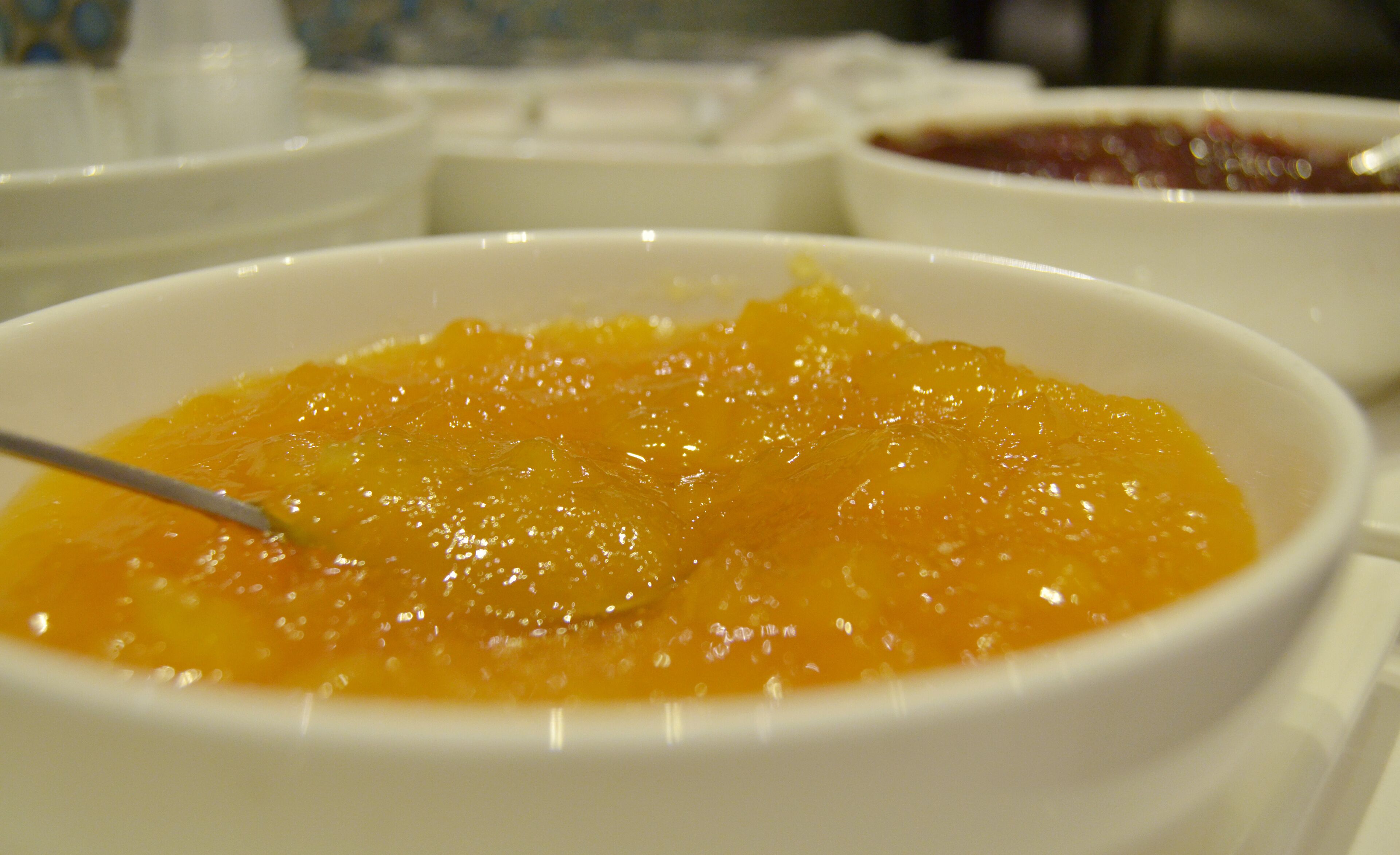 Ein Nahaufnahme einer Schüssel mit orangenem Fruchtkompott und einem Löffel.
