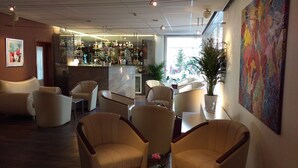 A bar area with a variety of liquor bottles, a seating area with chairs, and a large abstract painting on the wall.
