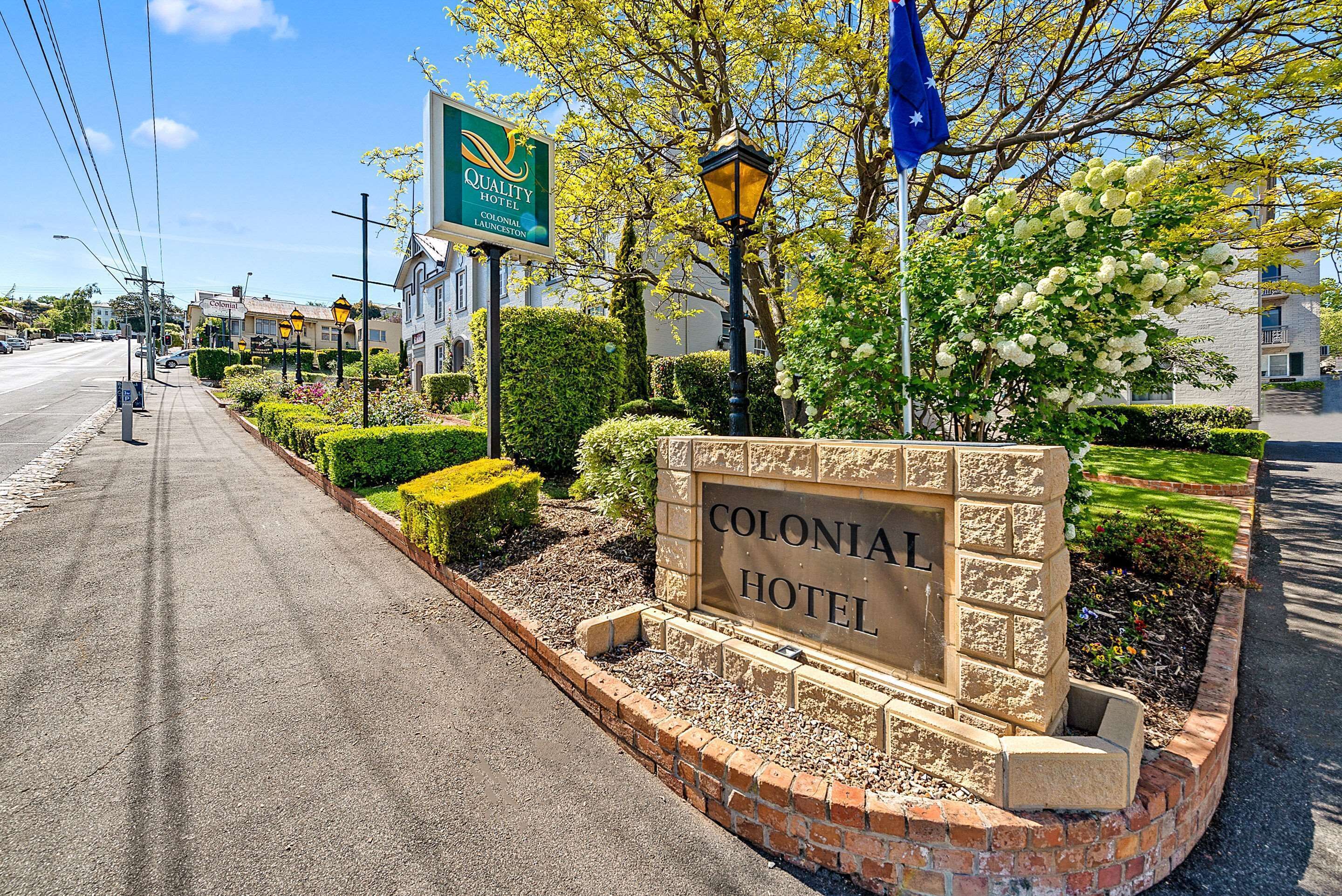 A Colonial Hotel sign with a brick border and a landscaped garden.