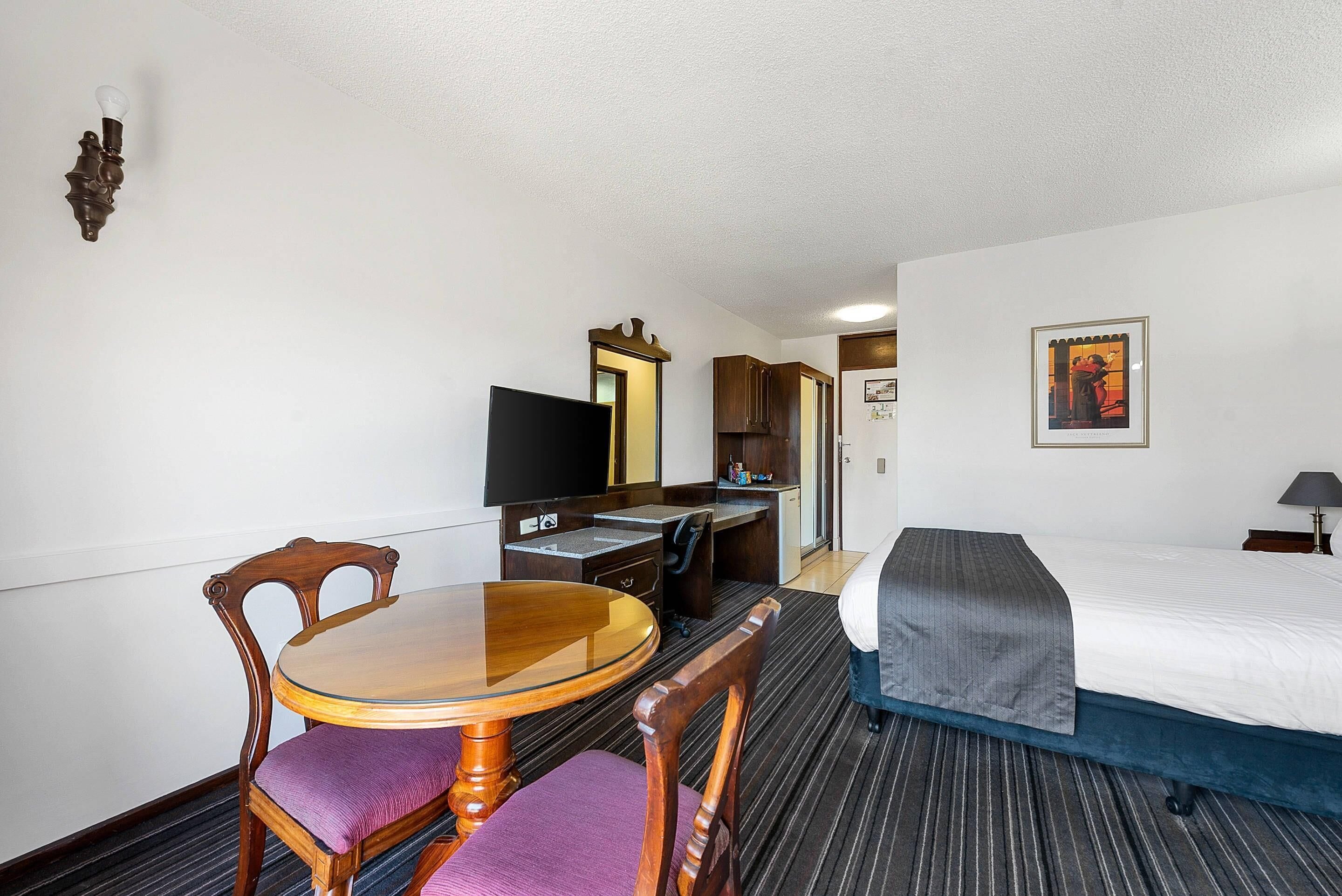 Une chambre d’hôtel comprenant un lit, un bureau avec un téléviseur à écran plat, une table à manger avec des chaises et une petite kitchenette.