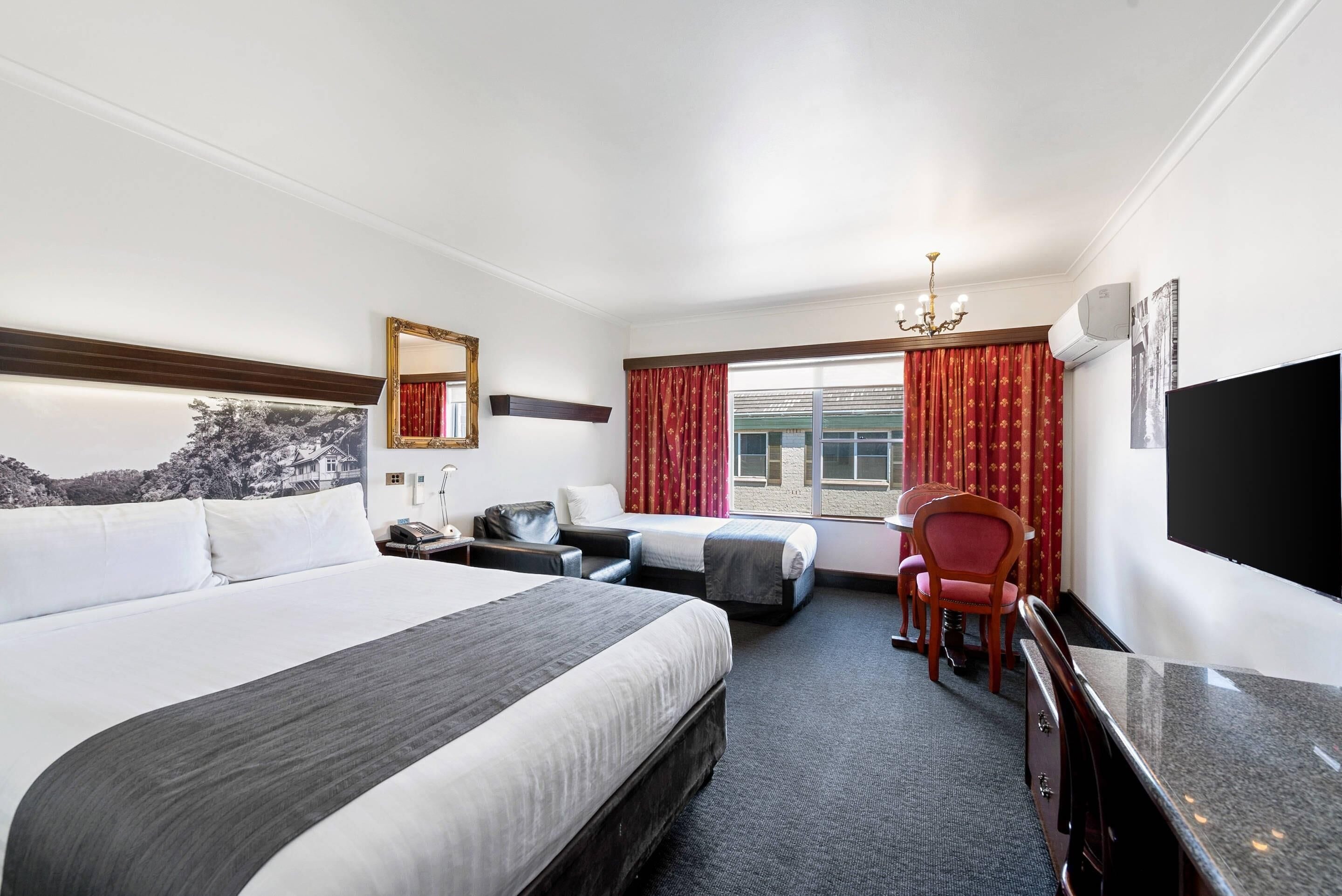 A hotel room with a large bed, a desk, a chair, a TV, and a window with curtains.