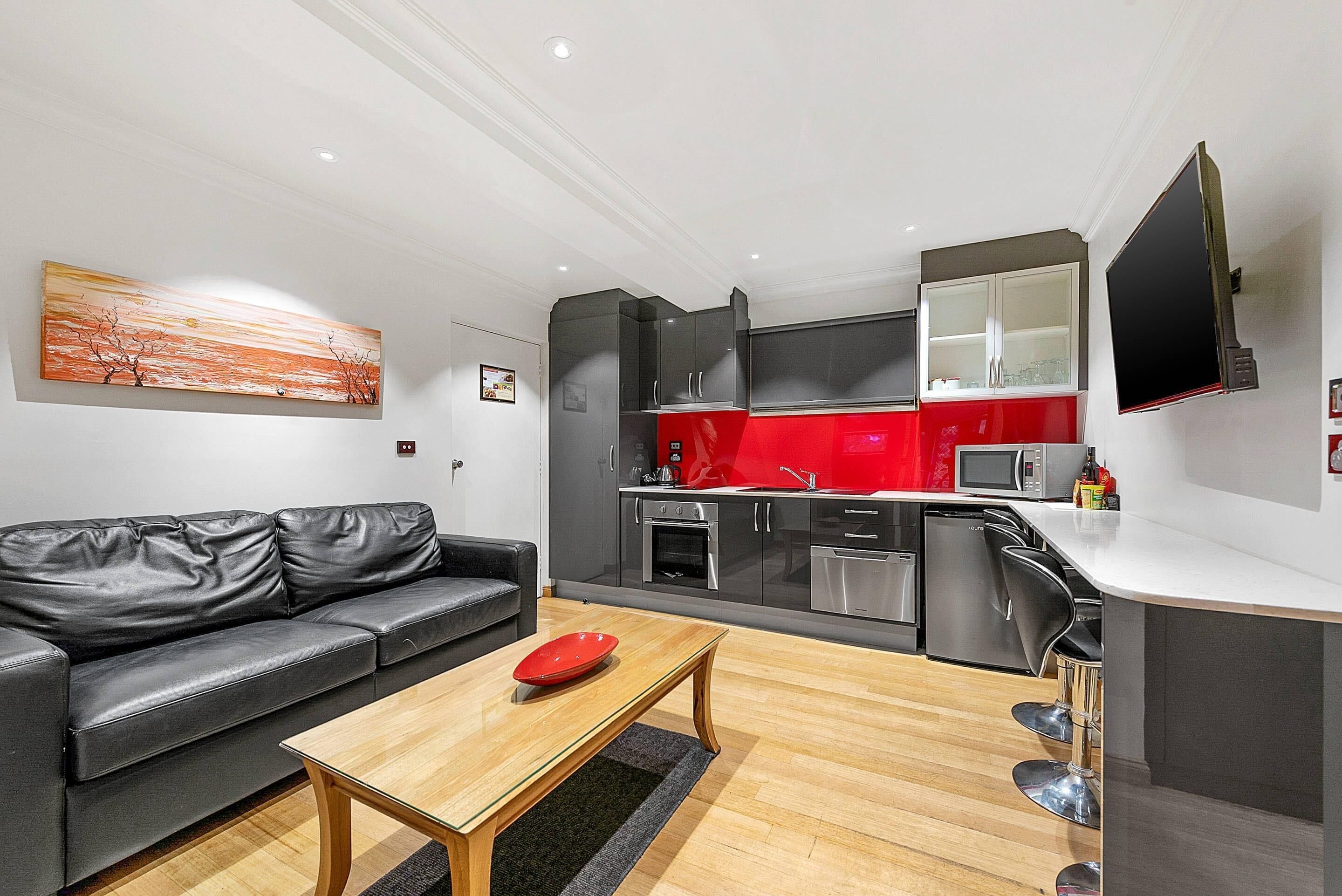 A modern kitchen with a red backsplash, a black sofa, and a flat-screen TV mounted on the wall.