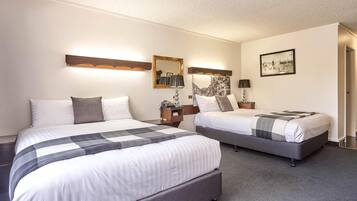 A hotel room with two beds, a nightstand with a lamp, a wall-mounted mirror, and a framed picture.