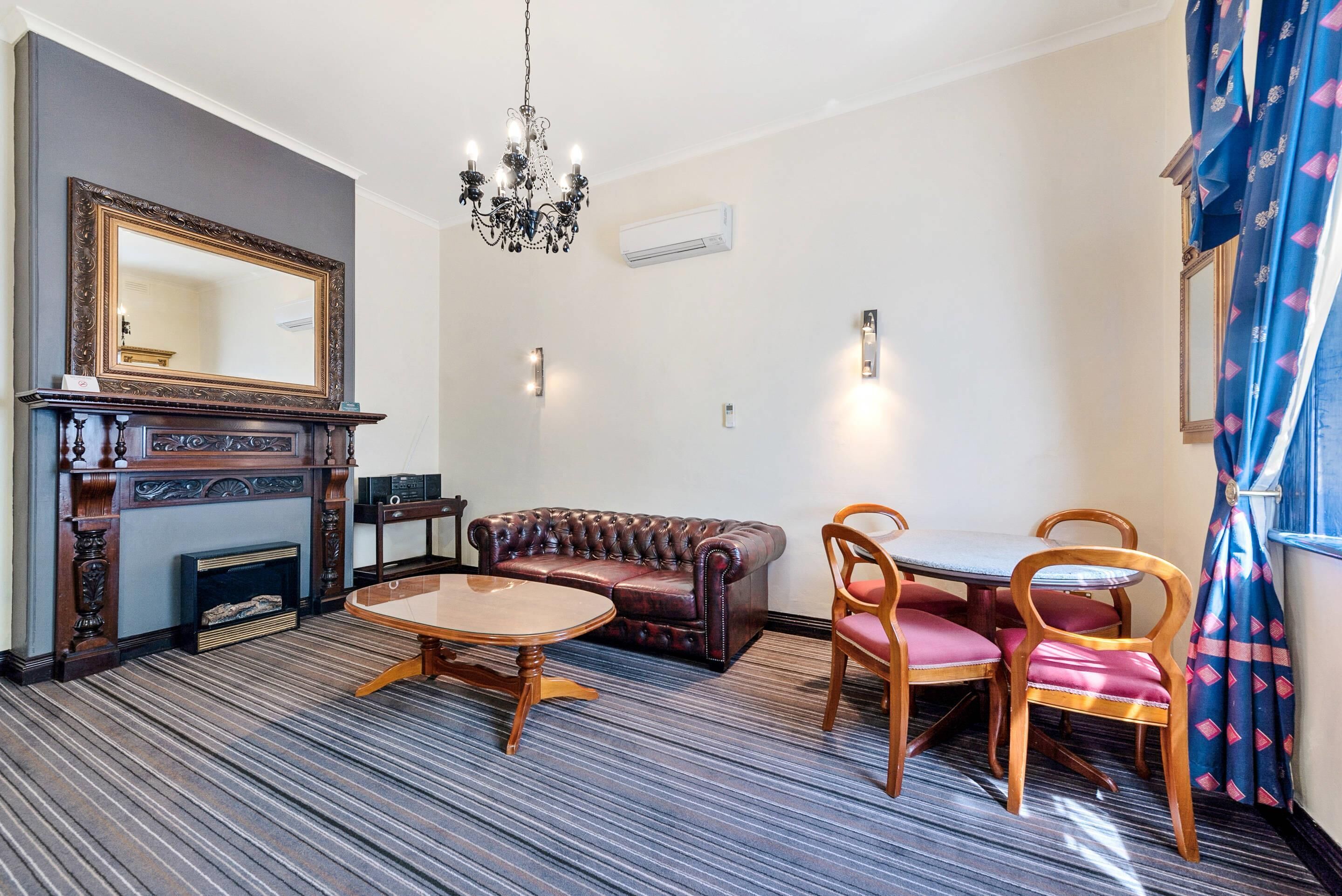 A room with a fireplace, a sofa, a dining table with chairs, a chandelier, and a large mirror.